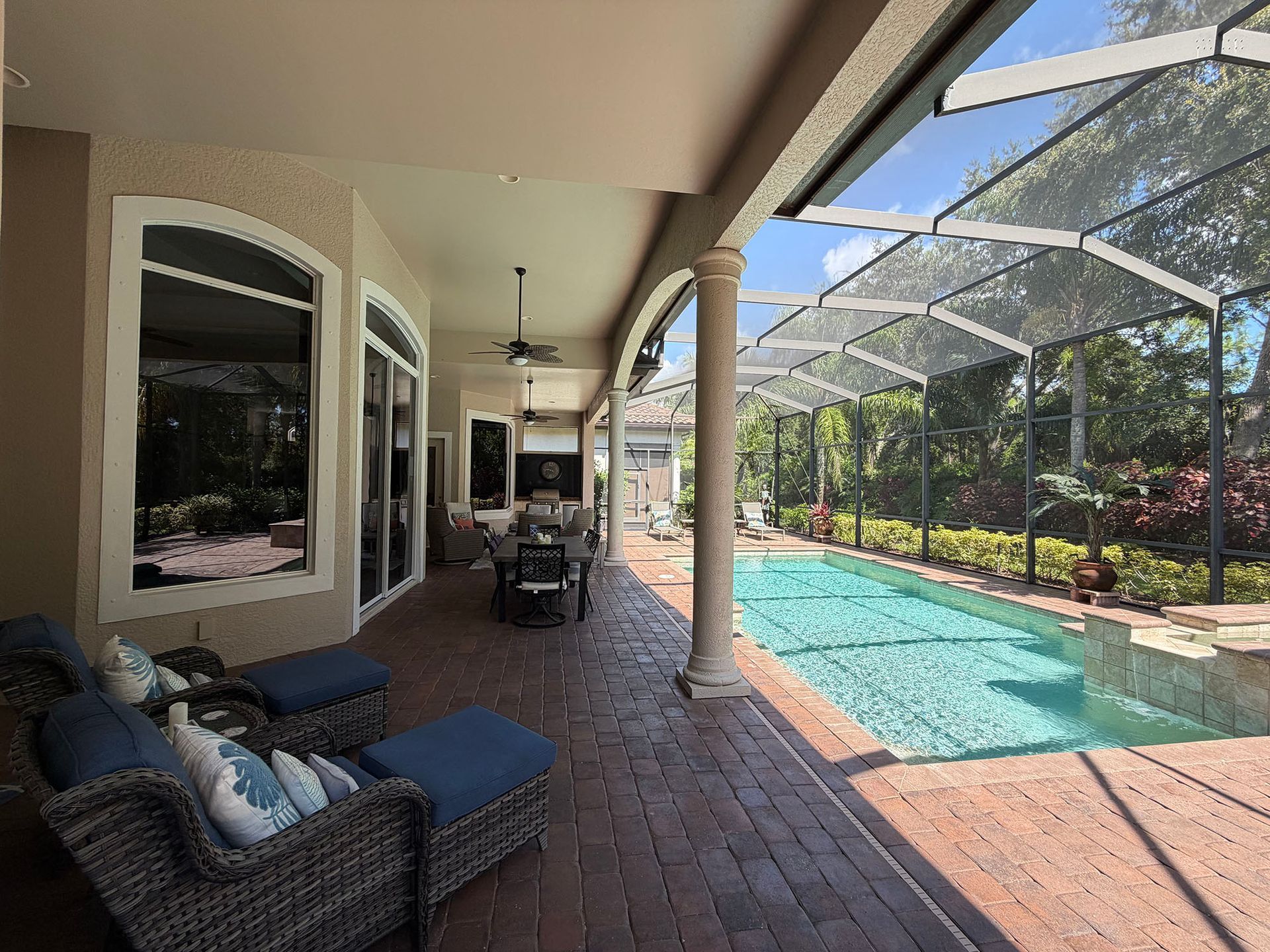 Covered patio with wicker loungers beside a brick pool deck and a narrow turquoise swimming pool.