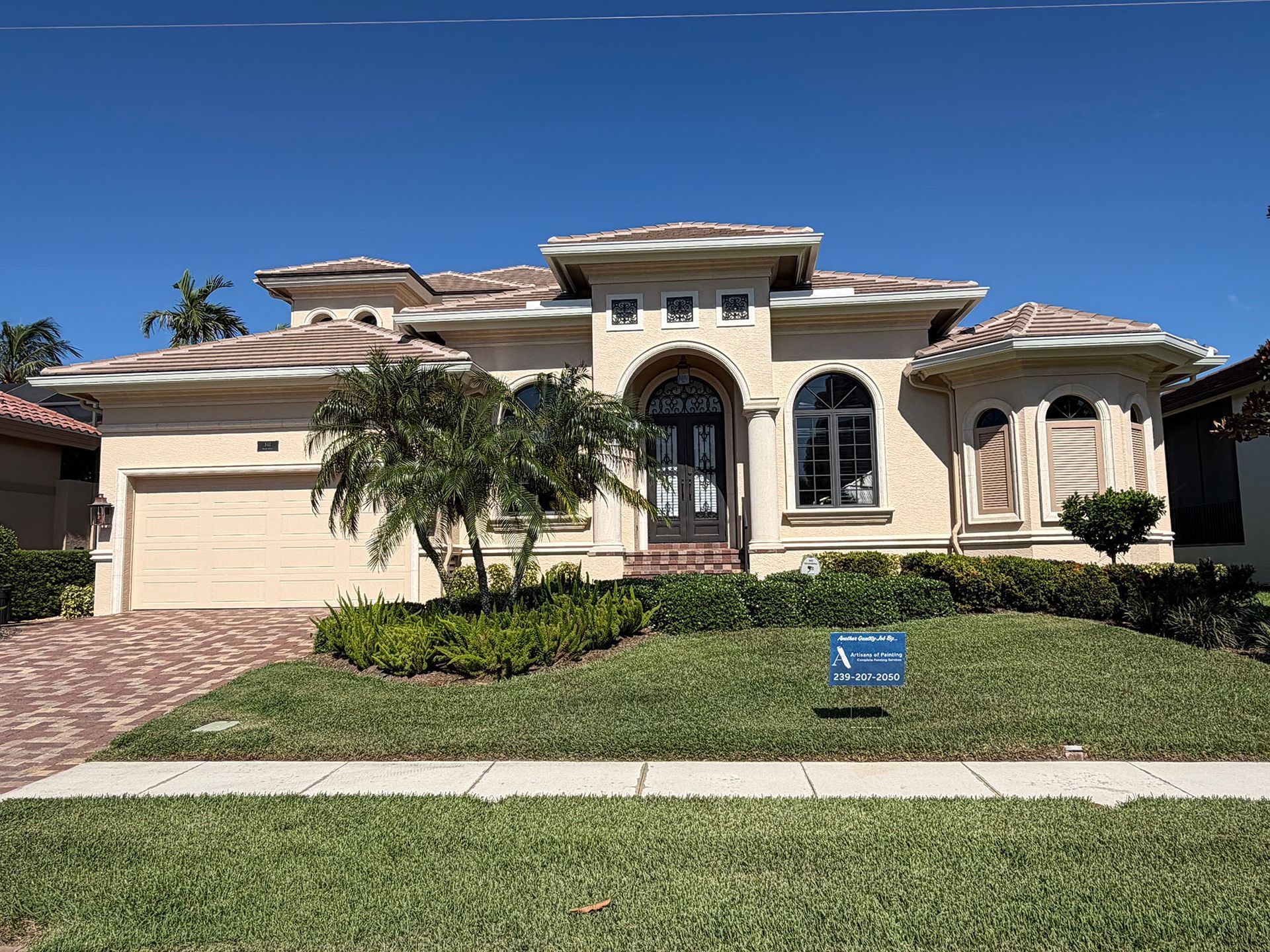 Single-story beige stucco house with a two-car garage, arched windows, and a landscaped front yard.