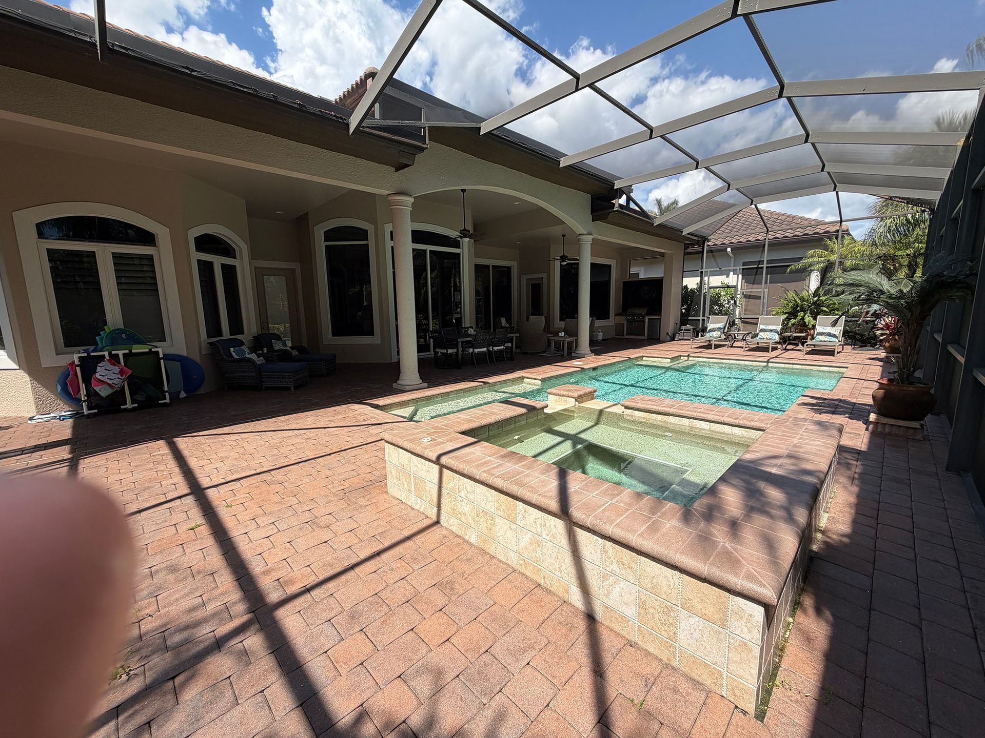 Backyard patio with a covered pool and hot tub beside a house, under a bright sky