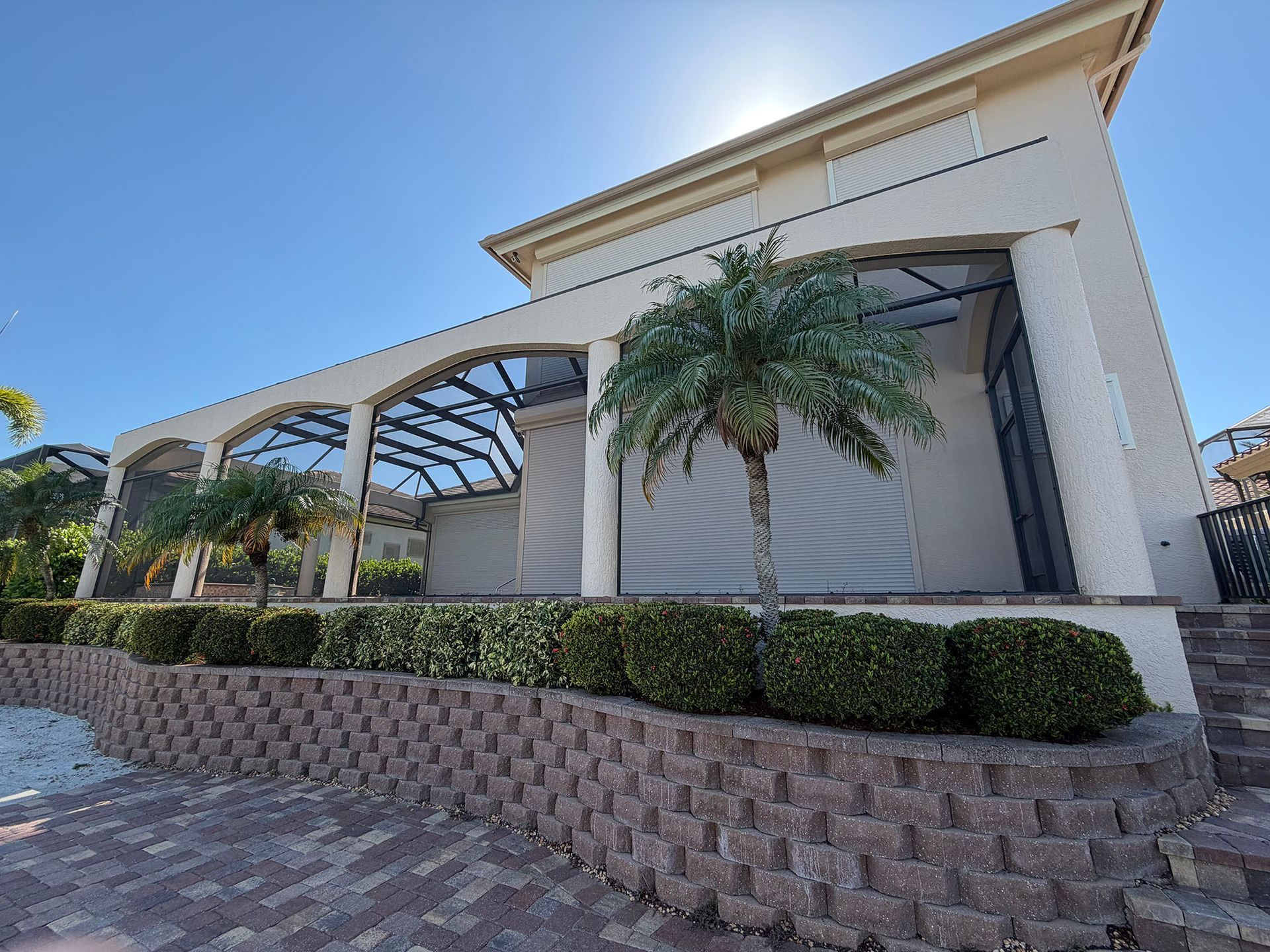 Modern white building with arched awnings, palm tree, and landscaped brick retaining wall.
