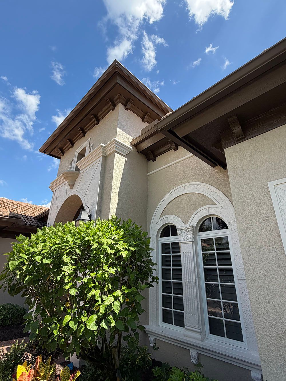 Exterior of a stucco house with arched windows, a tile roof, and green shrubbery under a blue sky