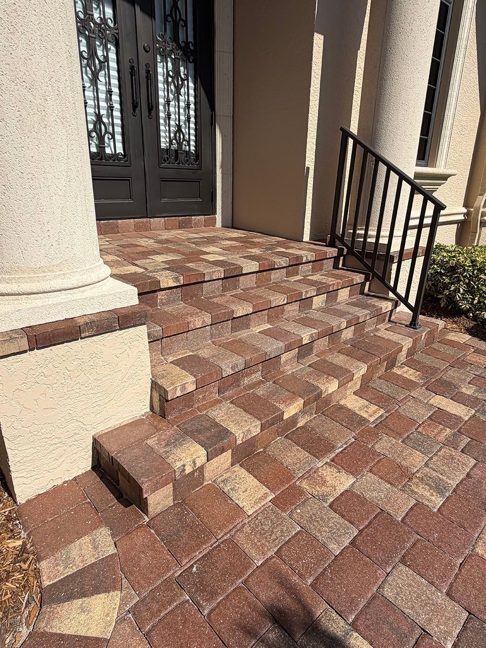 Brick steps leading to a front door with columns and a small black railing