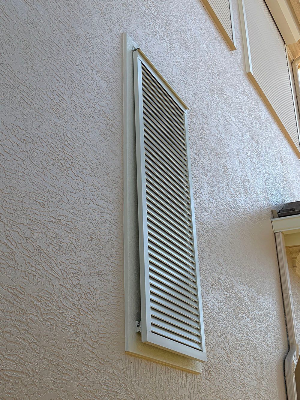 Tall white louvered vent on a beige stucco exterior wall, viewed from below.