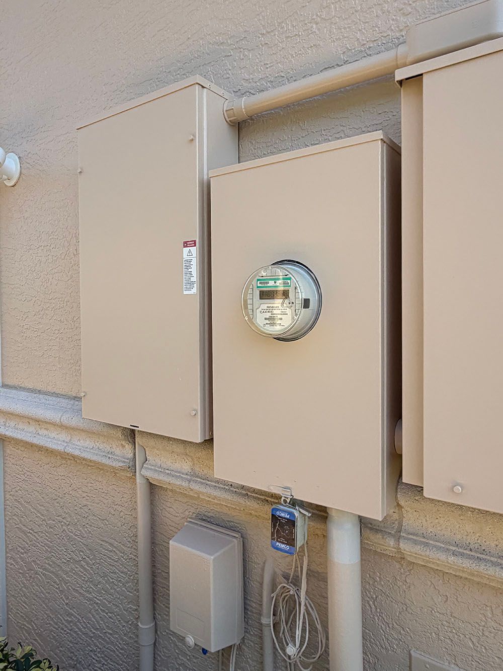 Beige utility meter boxes and electric meter mounted on an exterior stucco wall.