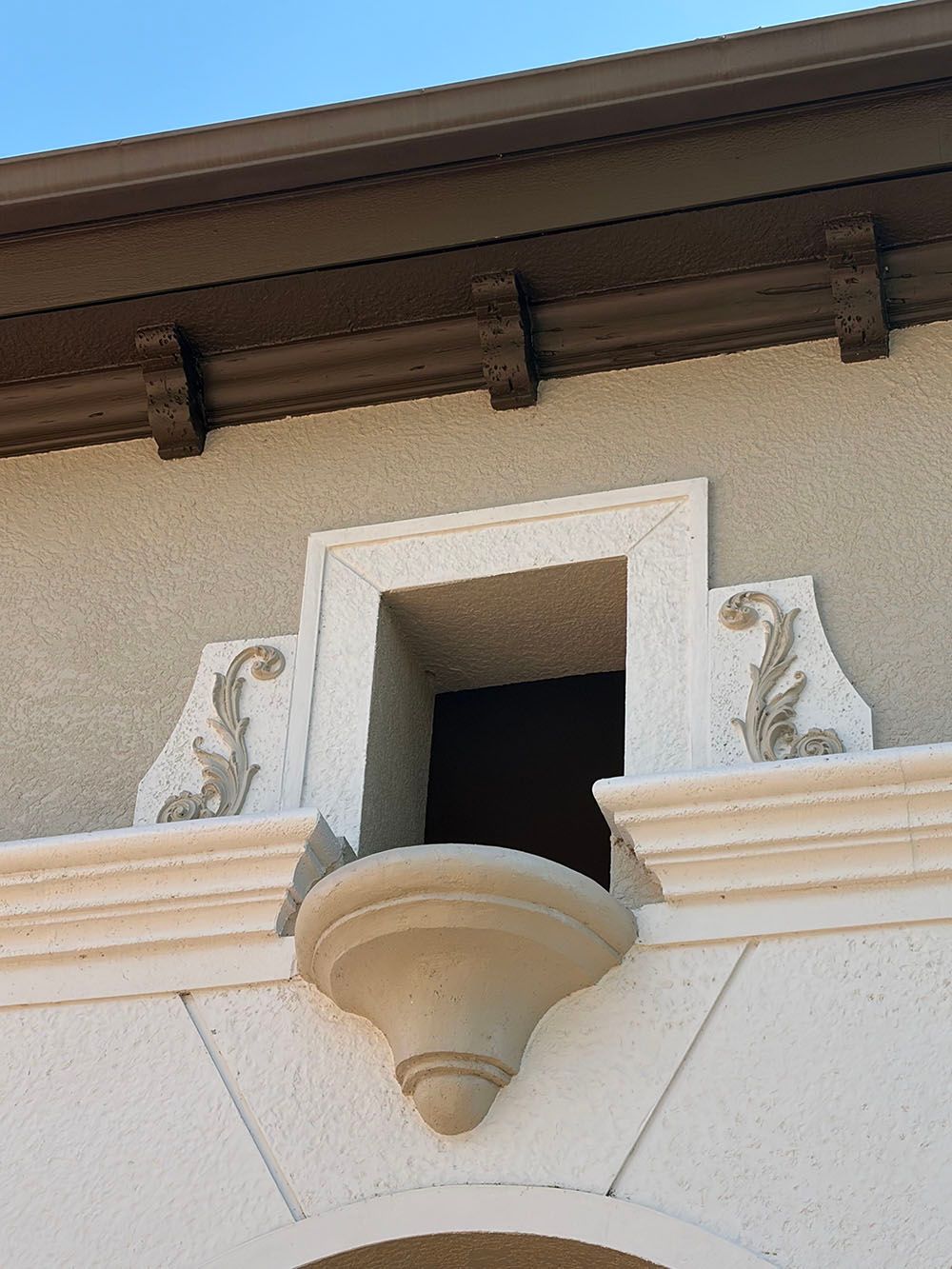 Ornate stucco window with white trim and decorative scrollwork on a beige building facade