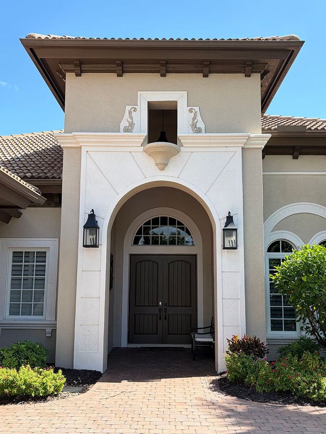 Front entrance of a Mediterranean-style house with arched doorway, white stucco, and a tiled roof.