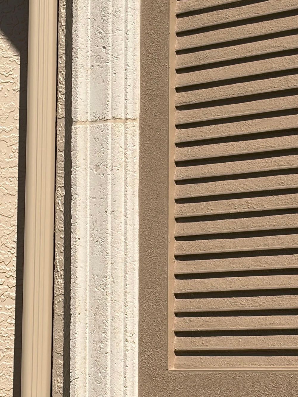 Close-up of a beige stucco wall with a louvered vent or shutter panel.