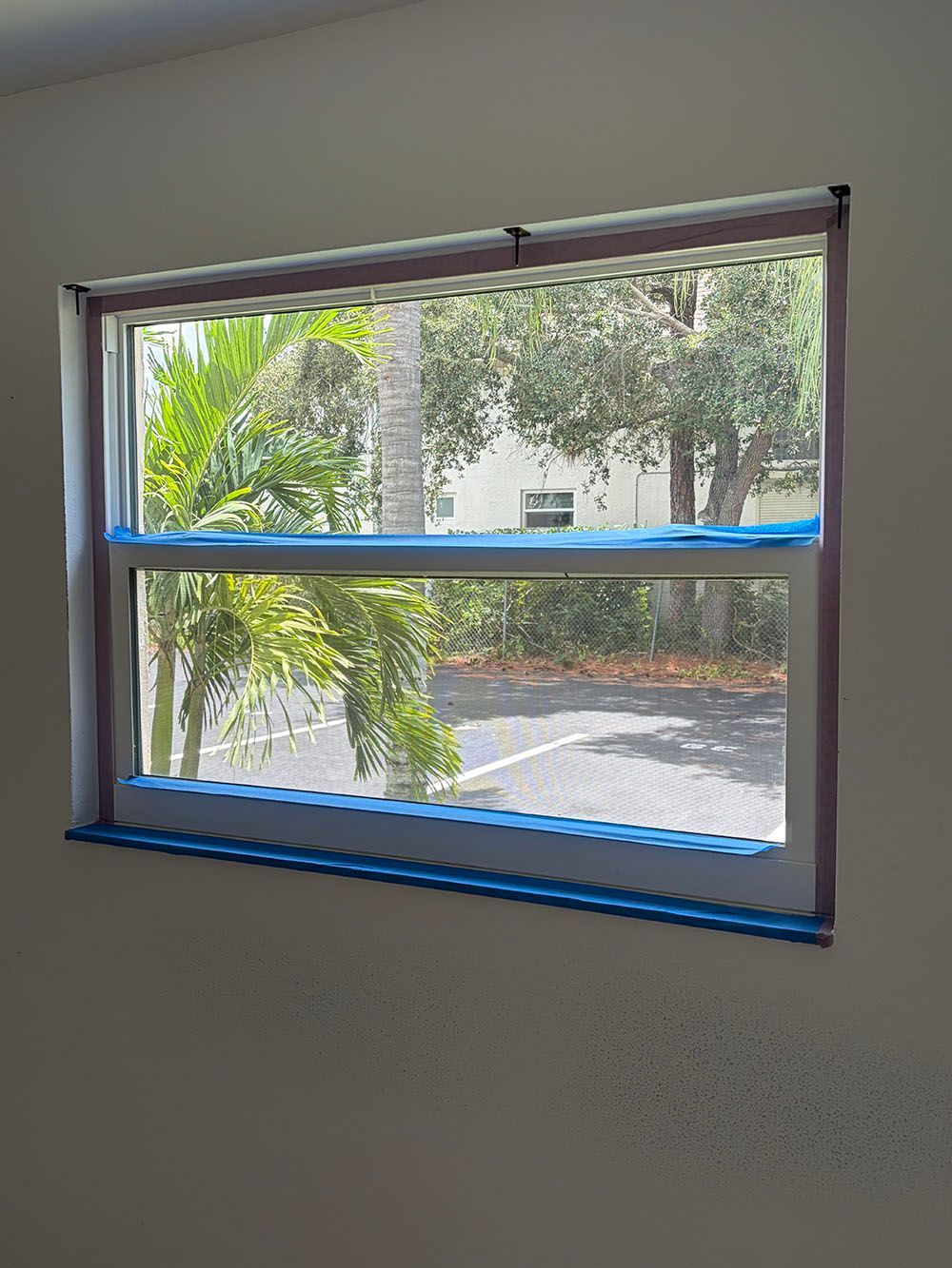Partially taped window with view of trees and a driveway outside