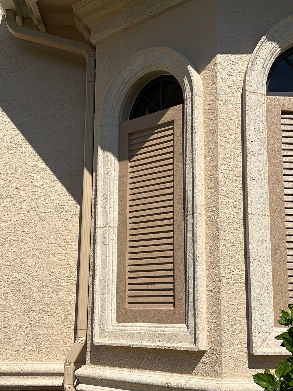 Beige stucco house exterior with arched windows and closed brown shutters.