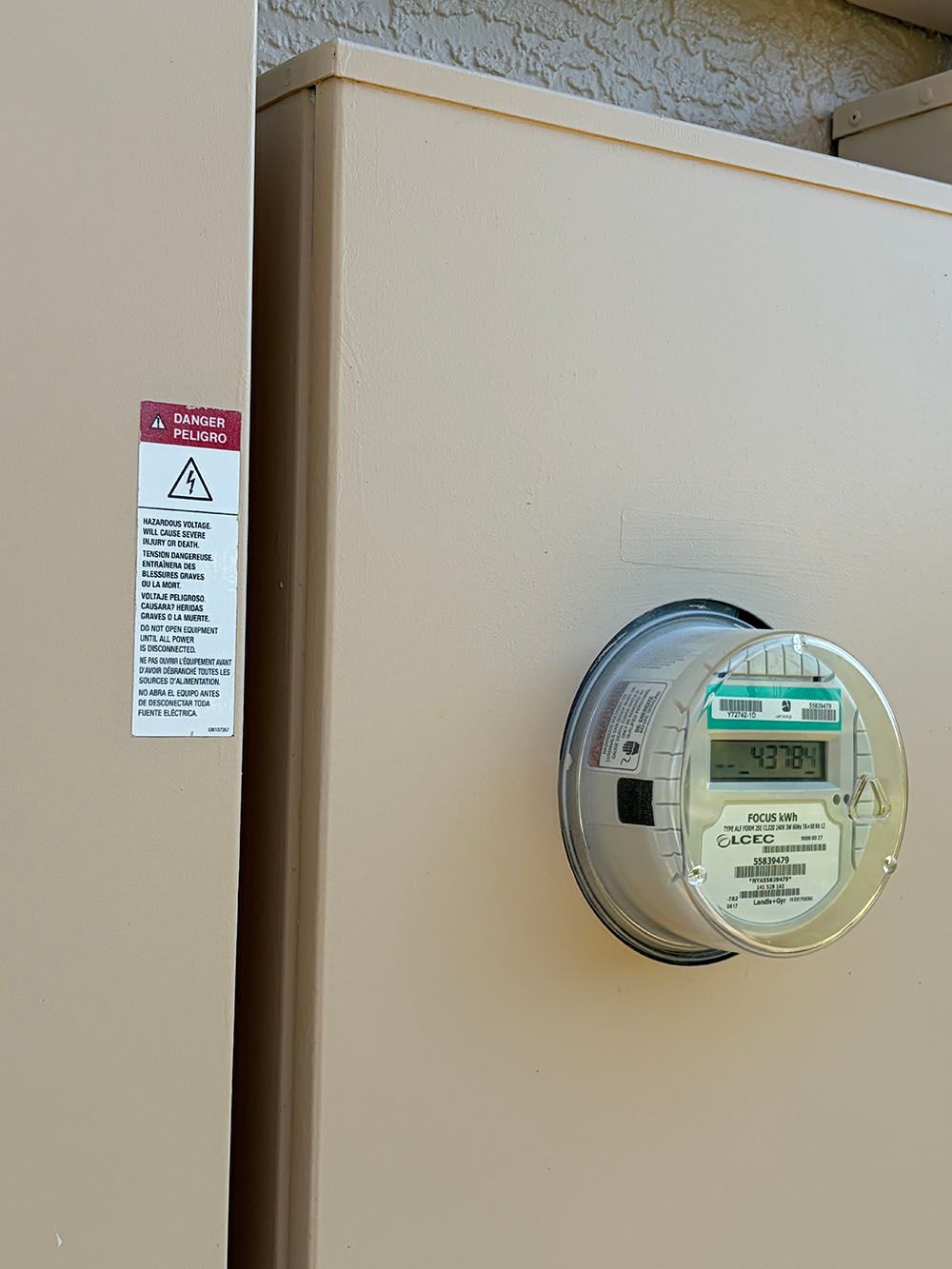 Utility meter on beige building wall with warning label