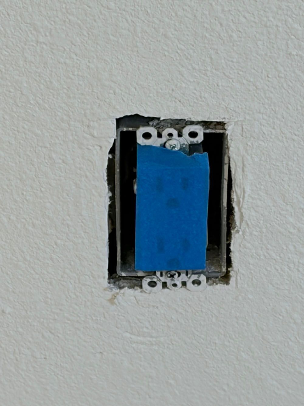 Blue electrical outlet box in a wall opening with exposed drywall edges
