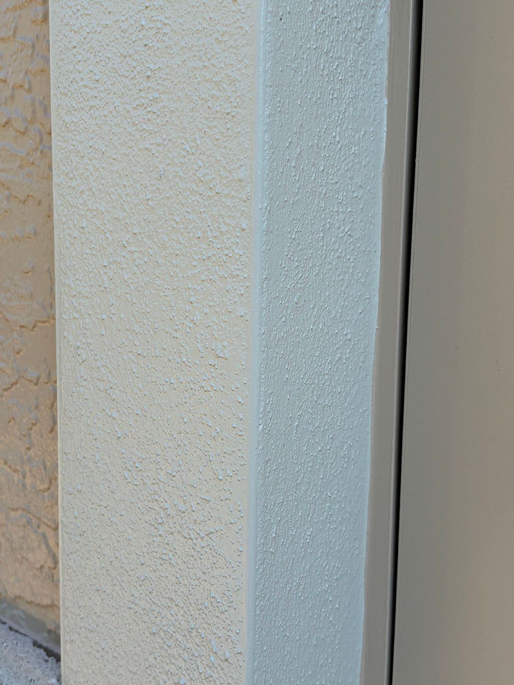 Close-up of a white textured wall corner with a light gray trim against a beige surface