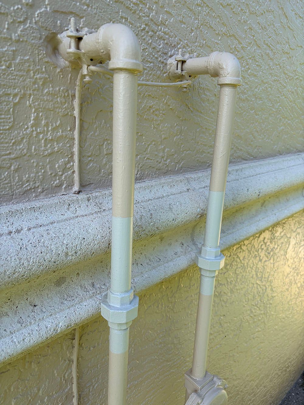 Two white outdoor pipes with valves mounted on a stucco wall above a concrete ledge