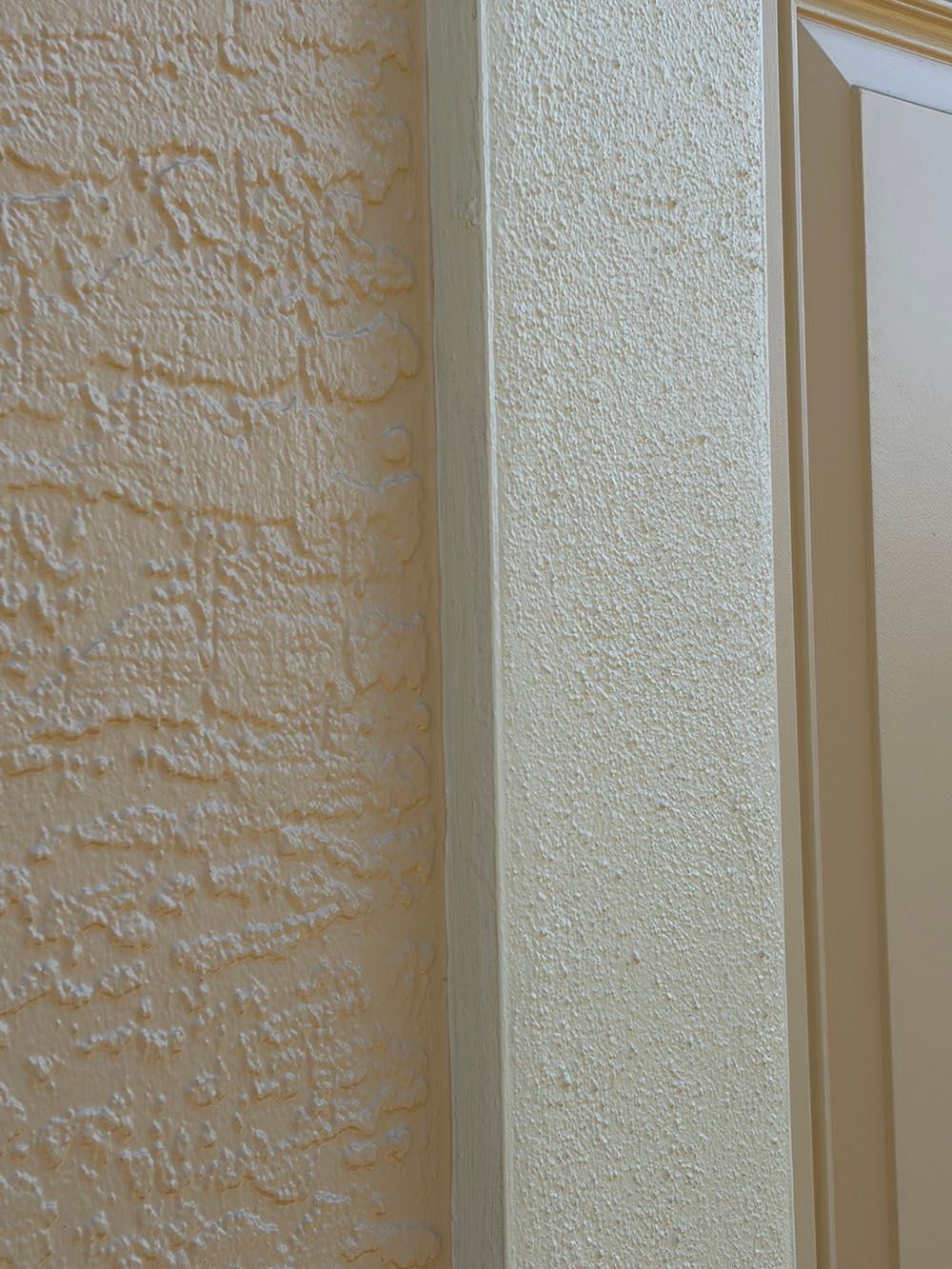 Close-up of a beige stucco wall next to a textured cream column and door frame.