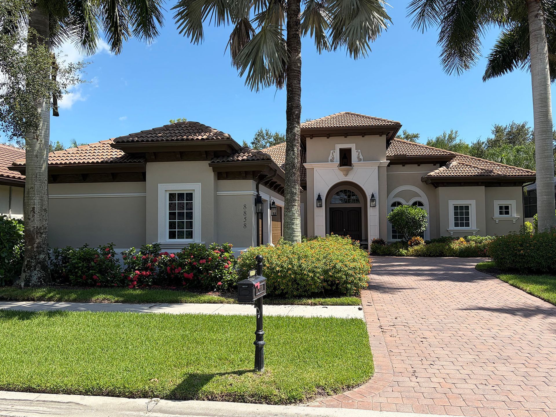 Large Mediterranean-style house with a red-tile roof, front lawn, palm trees, and a brick driveway.
