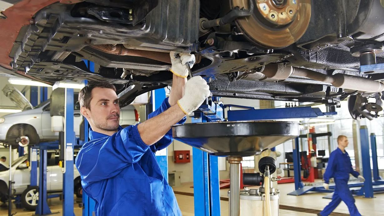 Mechanic in blue coveralls working under a raised car in an auto repair shop