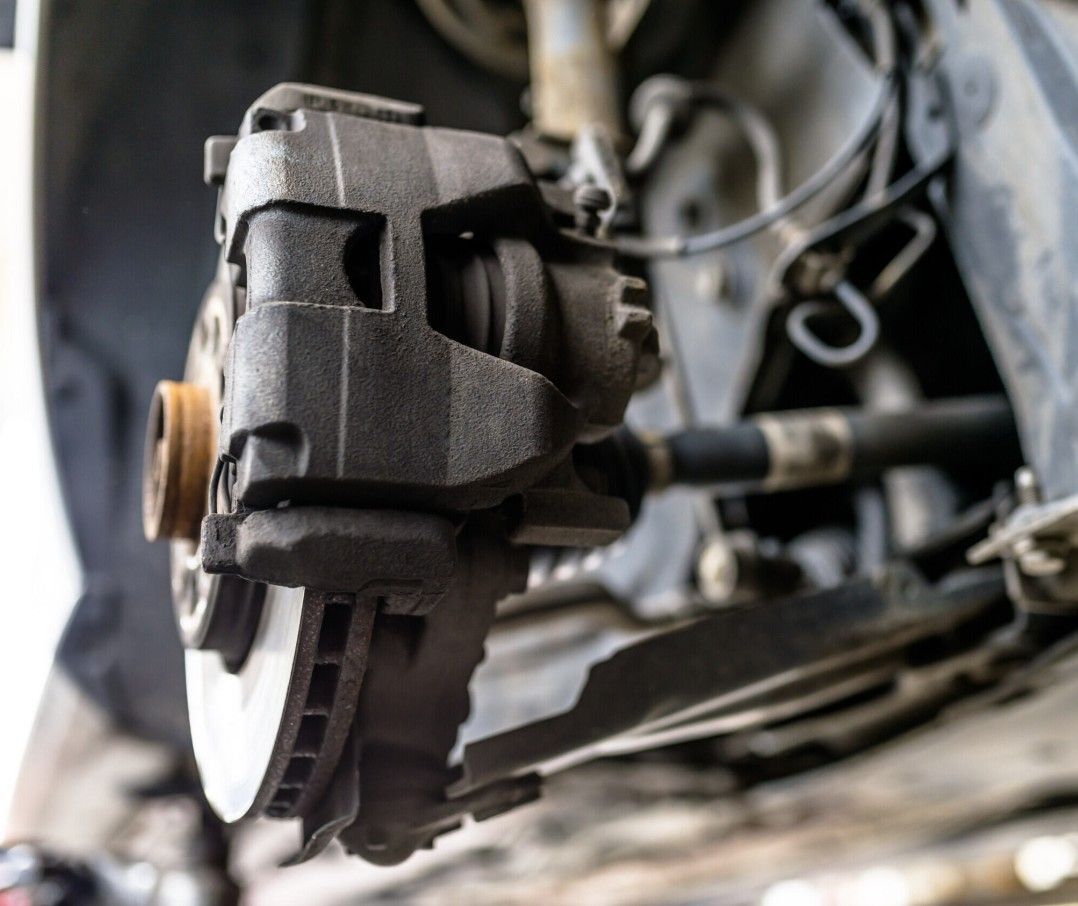Close-up of a car brake caliper and rotor with suspension components visible.