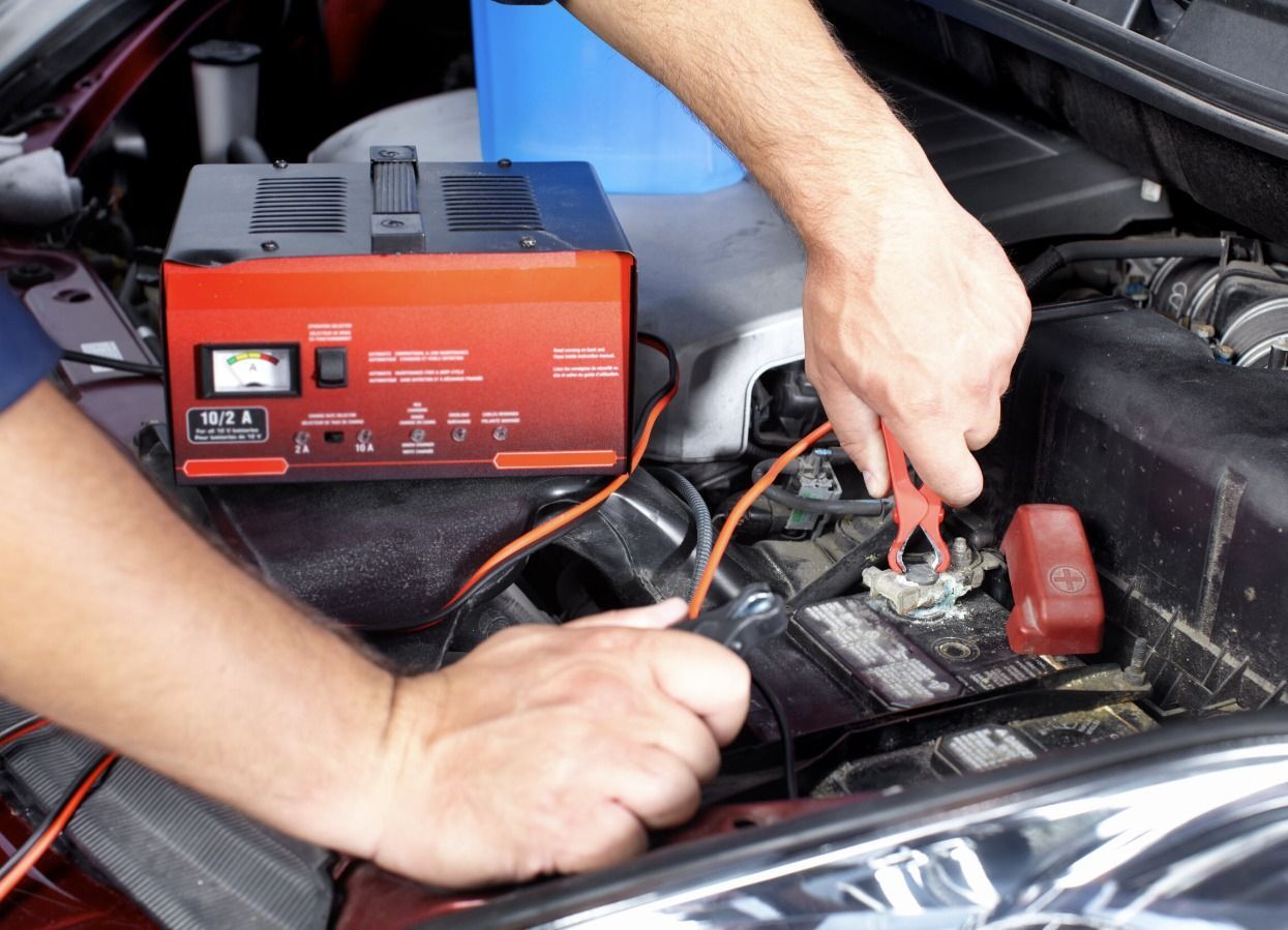 Person jump-starting a car battery with a red battery charger under the hood