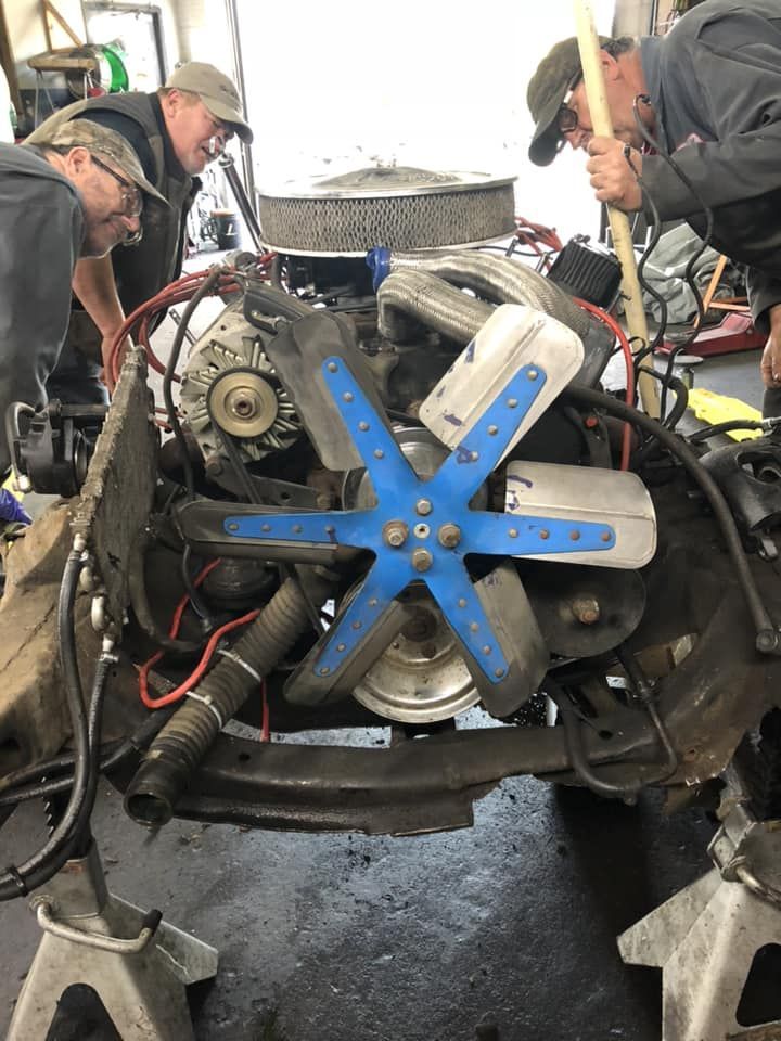Mechanics working on a car engine with a blue cooling fan in the foreground