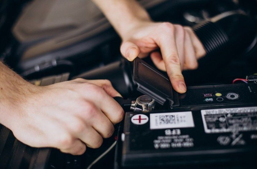 Hands connecting jumper cables to a car battery in a vehicle engine bay