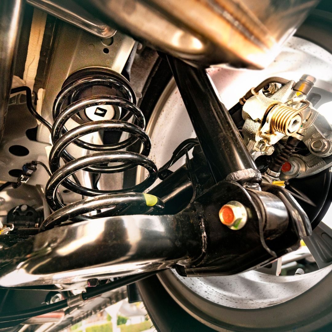 Close-up of a motorcycle rear suspension, black spring and chrome parts, with wheel and brake assembly visible