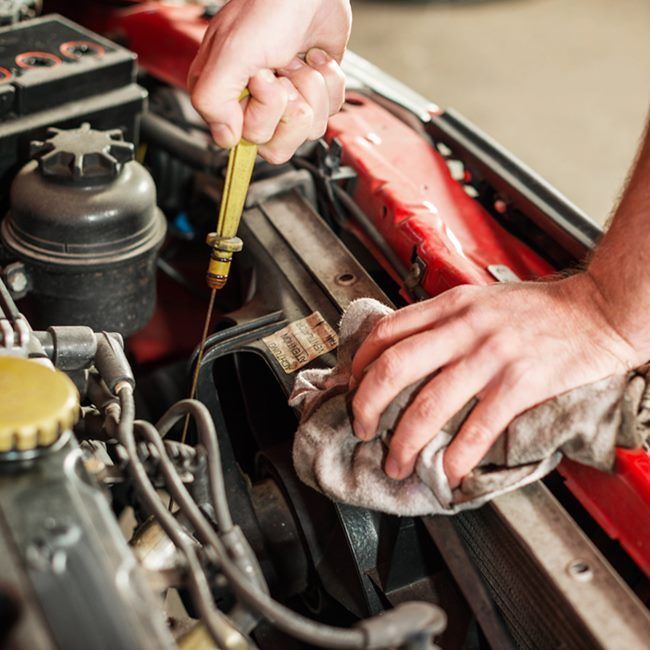 Mechanic checking a car engine with a dipstick and rag in a red vehicle's engine bay