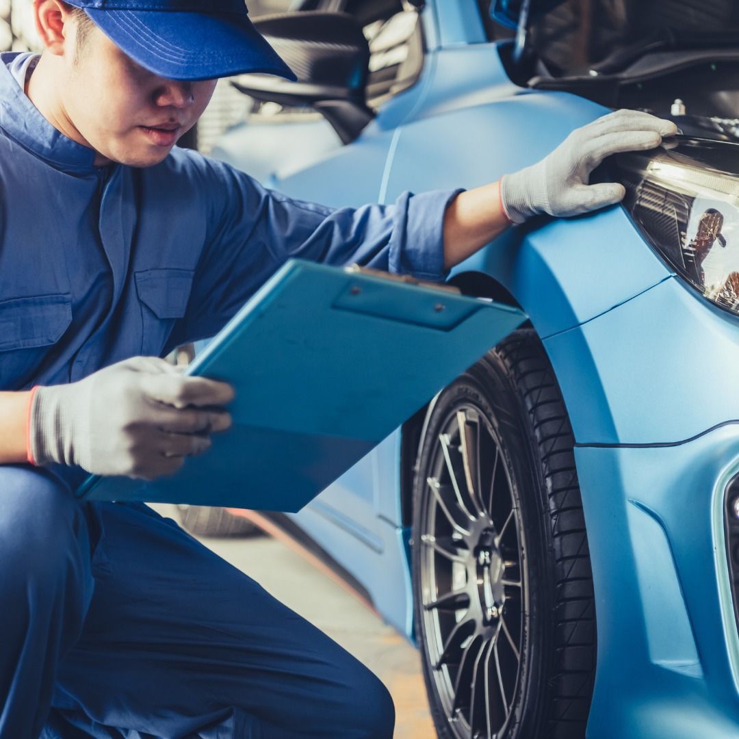 Mechanic in blue uniform inspecting a blue car with a clipboard in a garage