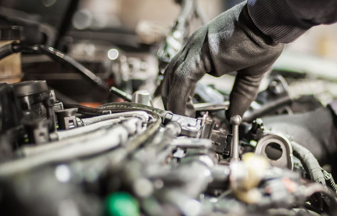 Mechanic’s gloved hands working on an engine bay with tools and hoses