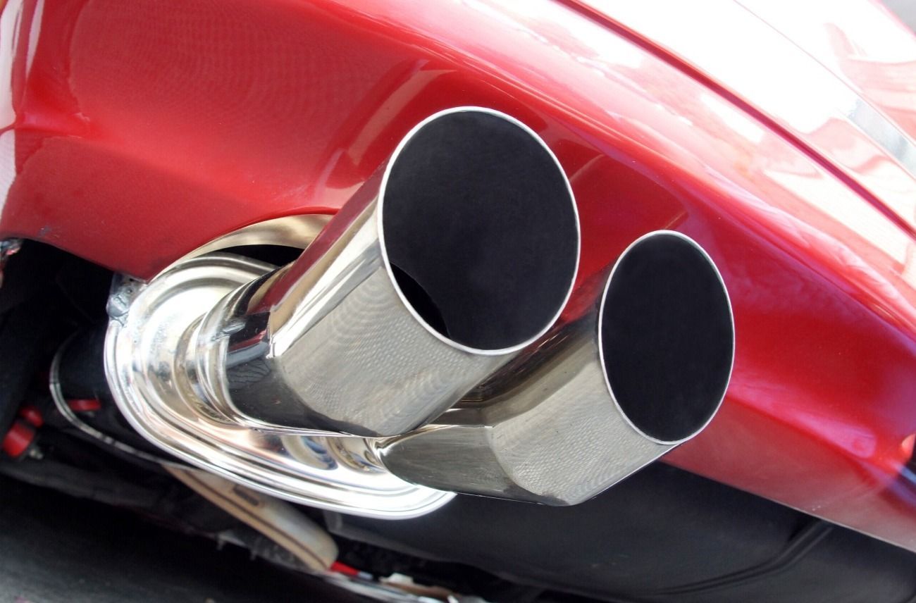 Close-up of twin chrome exhaust pipes beneath a red car bumper