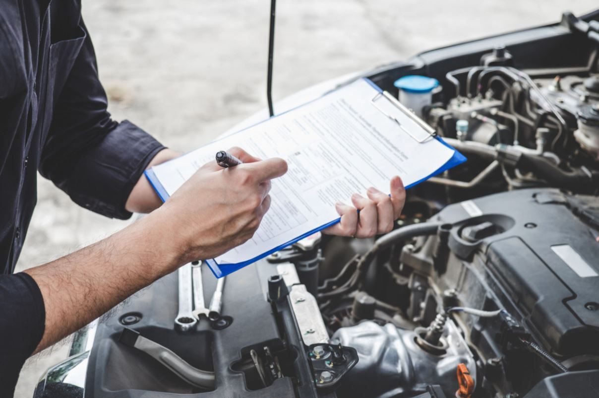 Mechanic filling out a checklist beside an open car engine in a garage