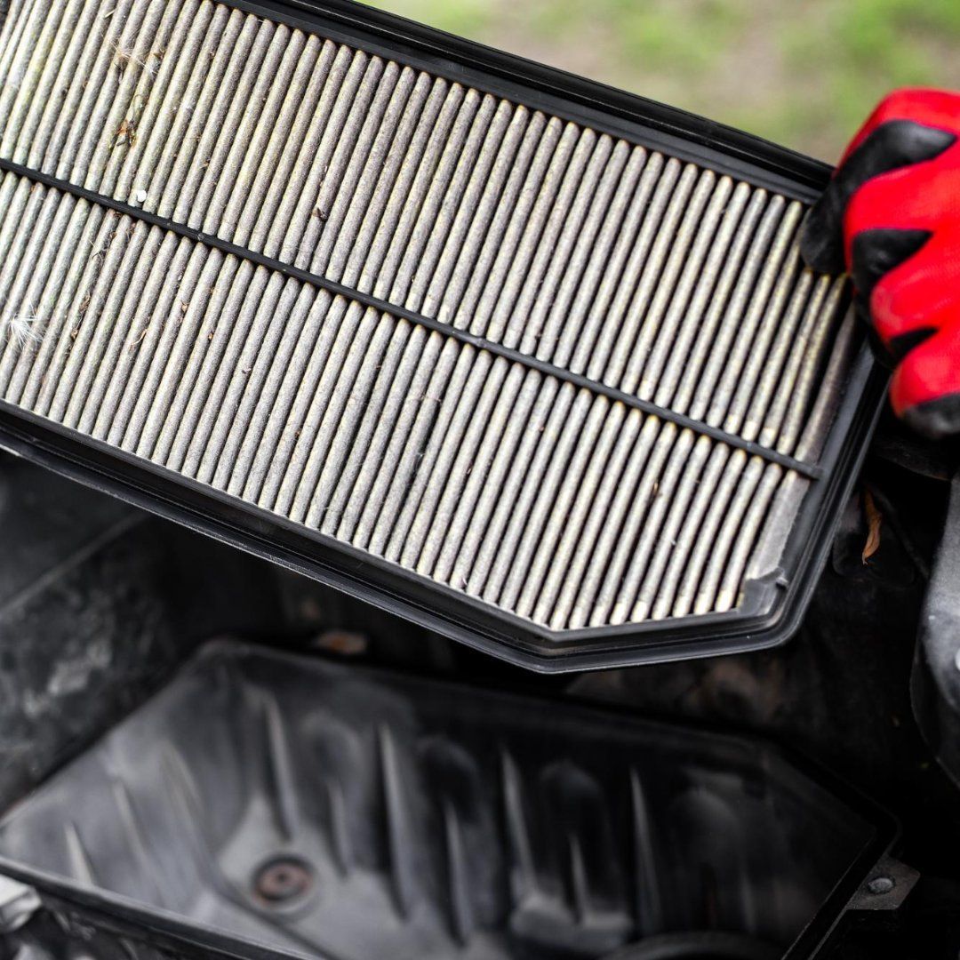 Person holding a dirty rectangular air filter above a black engine compartment