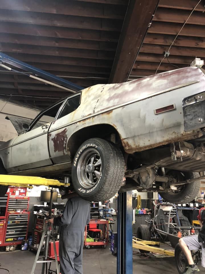 Rusty classic car lifted on a shop hoist in a busy auto repair garage