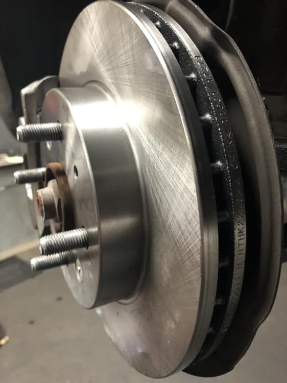 Close-up of a car brake rotor and caliper assembly with lug studs in a garage.