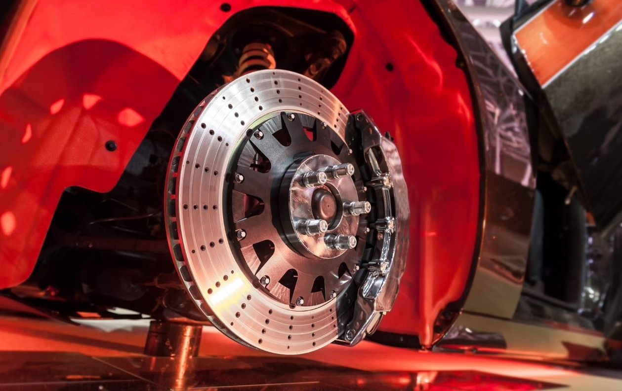 Close-up of a red sports car’s shiny brake rotor and wheel assembly under dramatic lighting