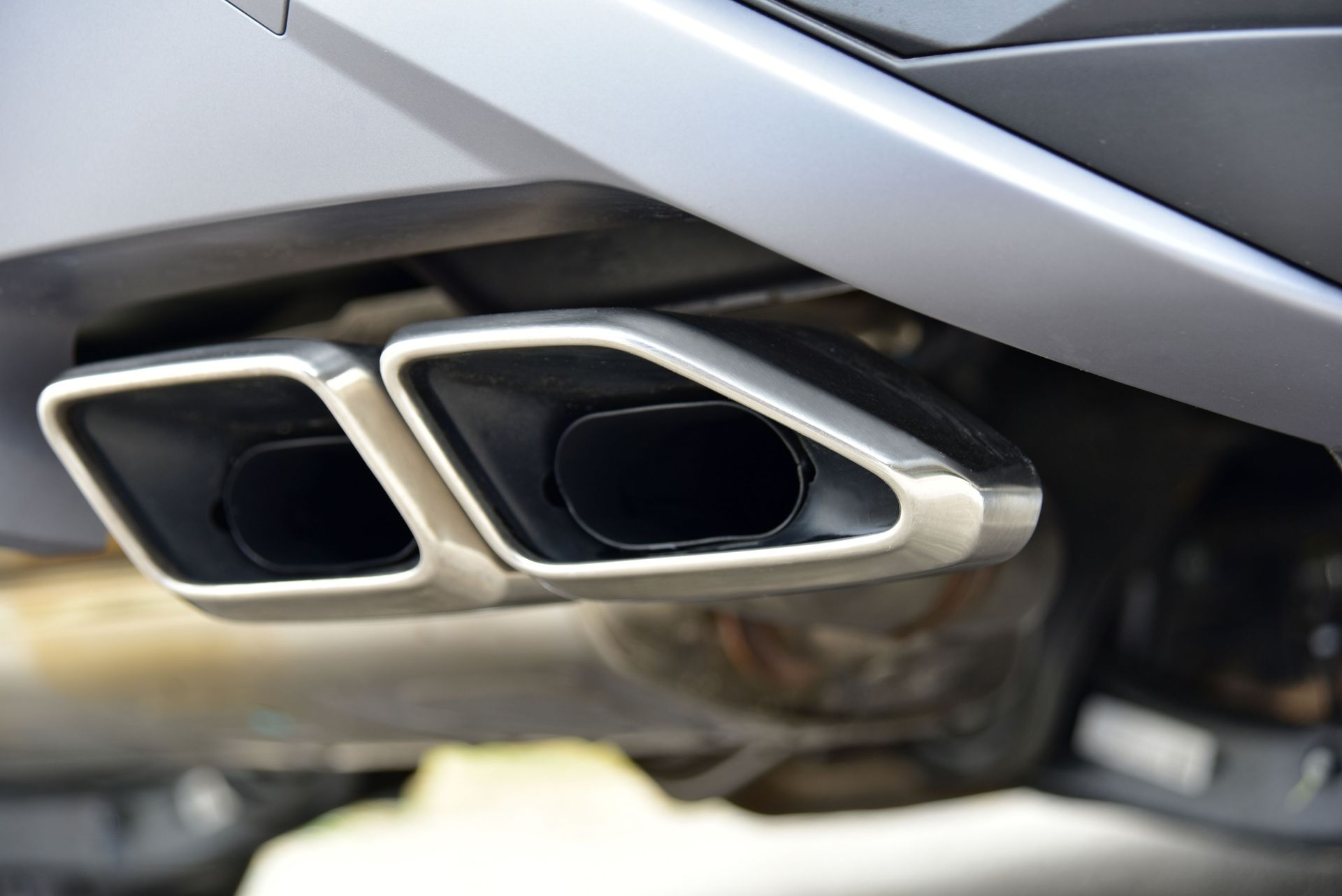 Close-up of dual chrome car exhaust tips beneath a silver bumper