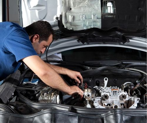 Mechanic in blue shirt working under a car hood in an auto repair shop