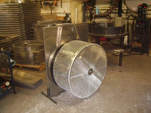 Metal industrial parts washer with rotating mesh drum and stainless steel housing in a workshop setting.