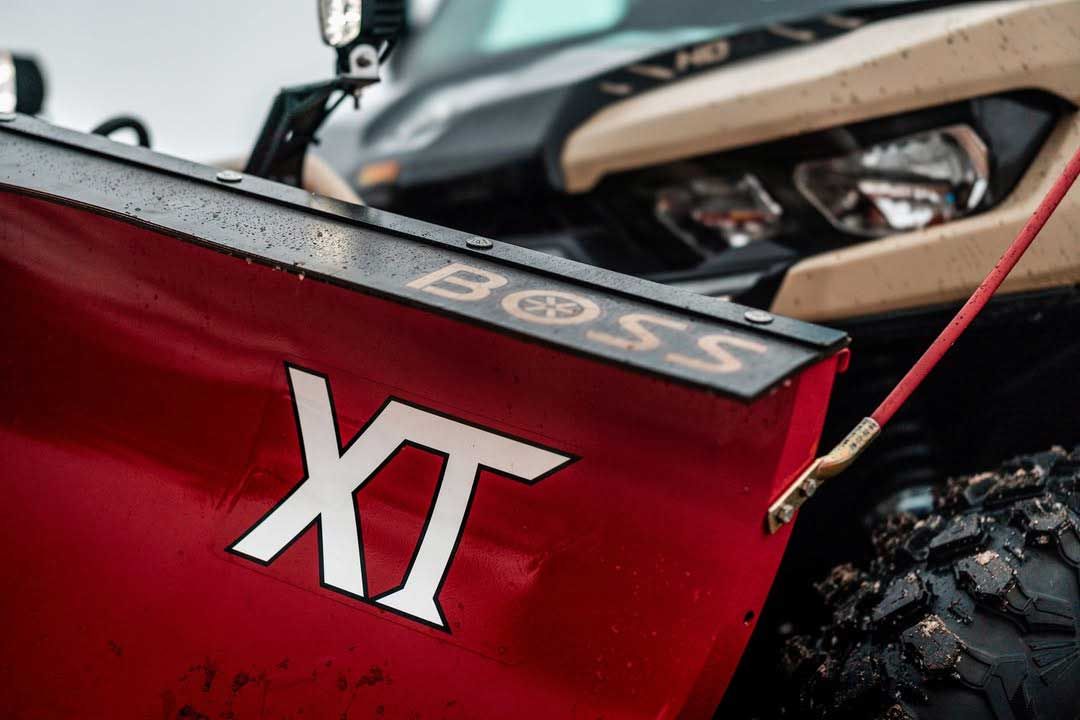Red BOSS XT snowplow attached to a tan and black UTV. The plow is angled slightly, ready for snow removal.