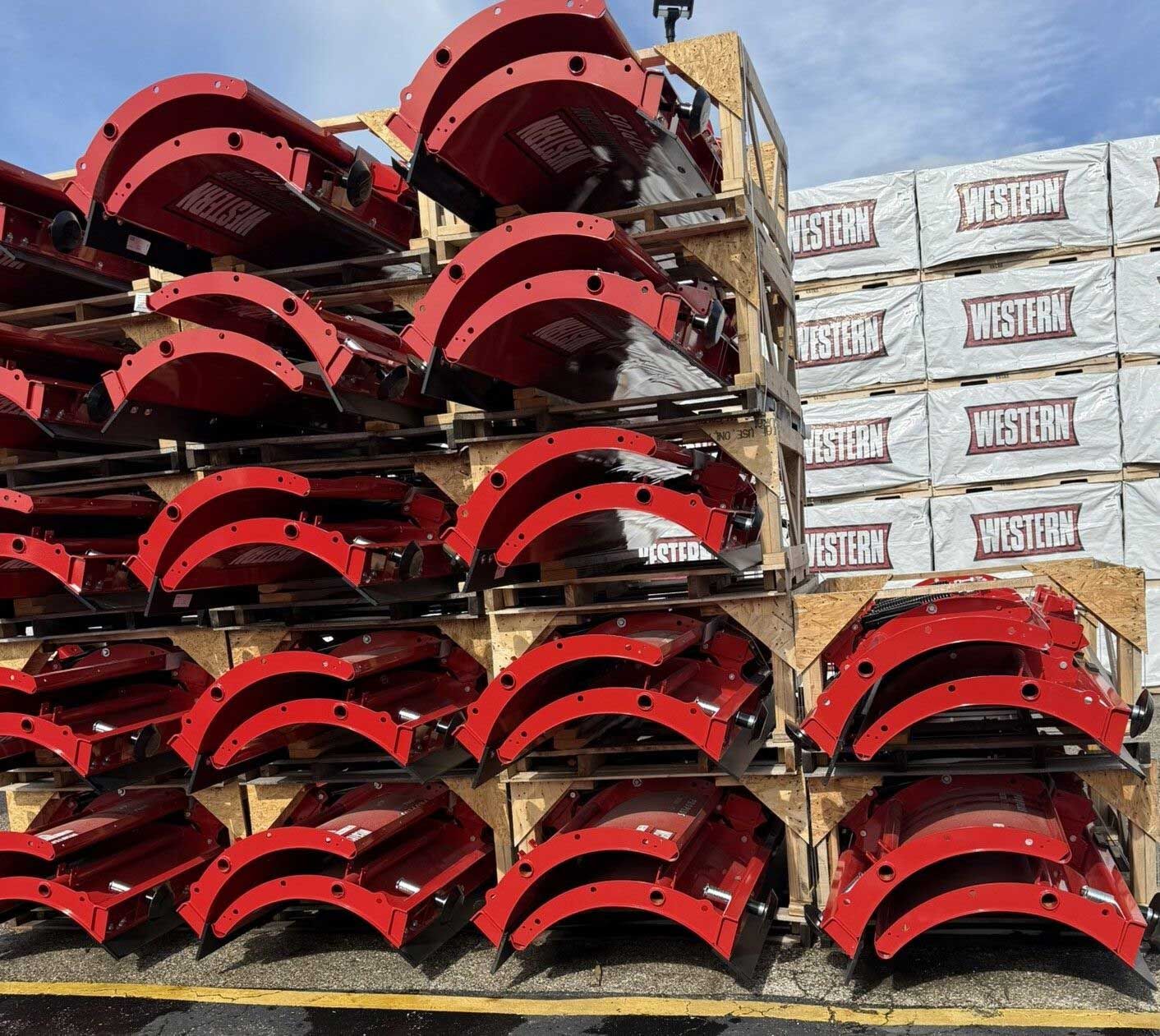 Stacks of red, curved metal structures on pallets with wooden planks in the background.
