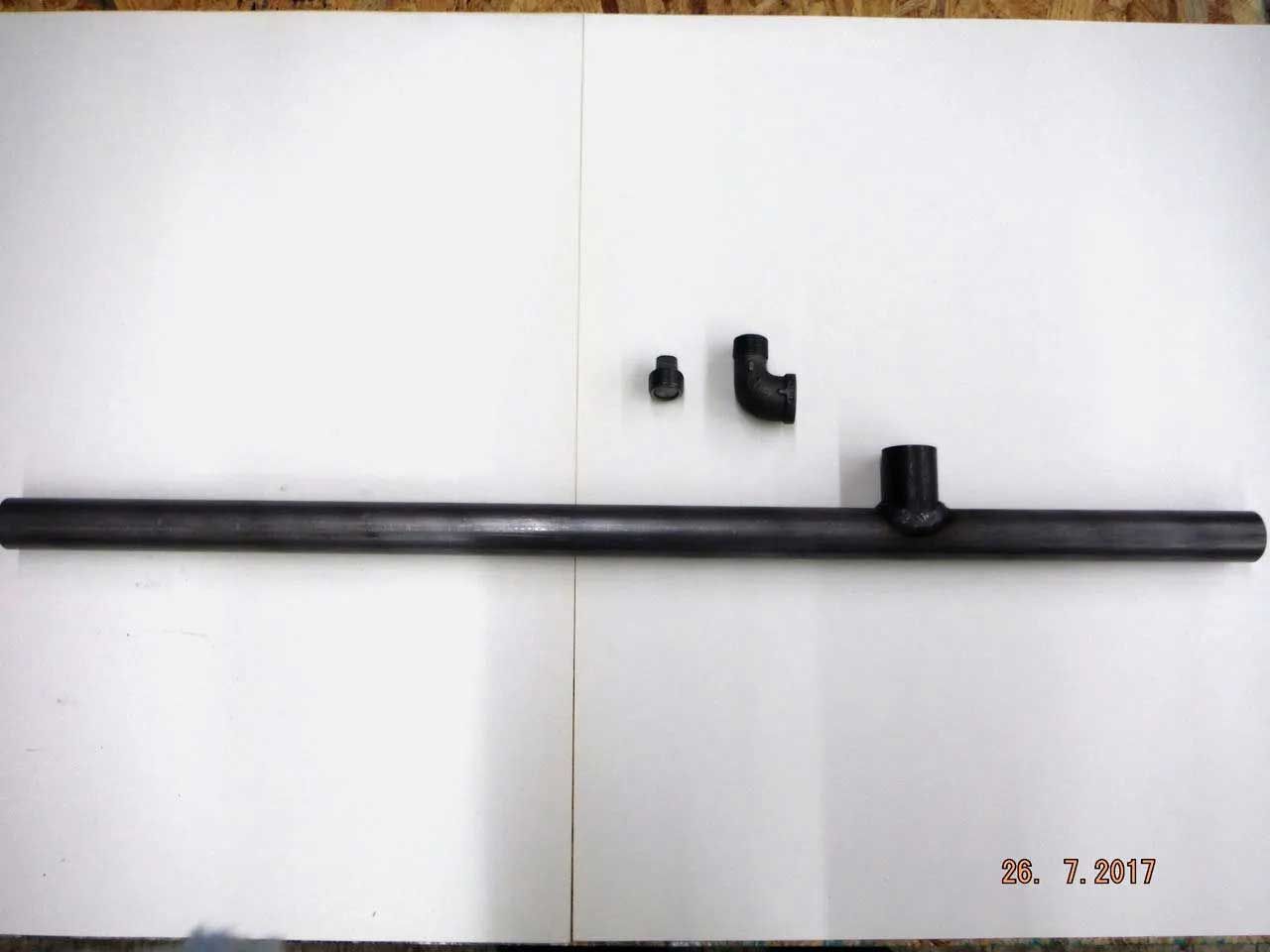 Black metal pipes and fittings on a white surface. The arrangement includes a long straight pipe, a small fitting, and two elbow joints.