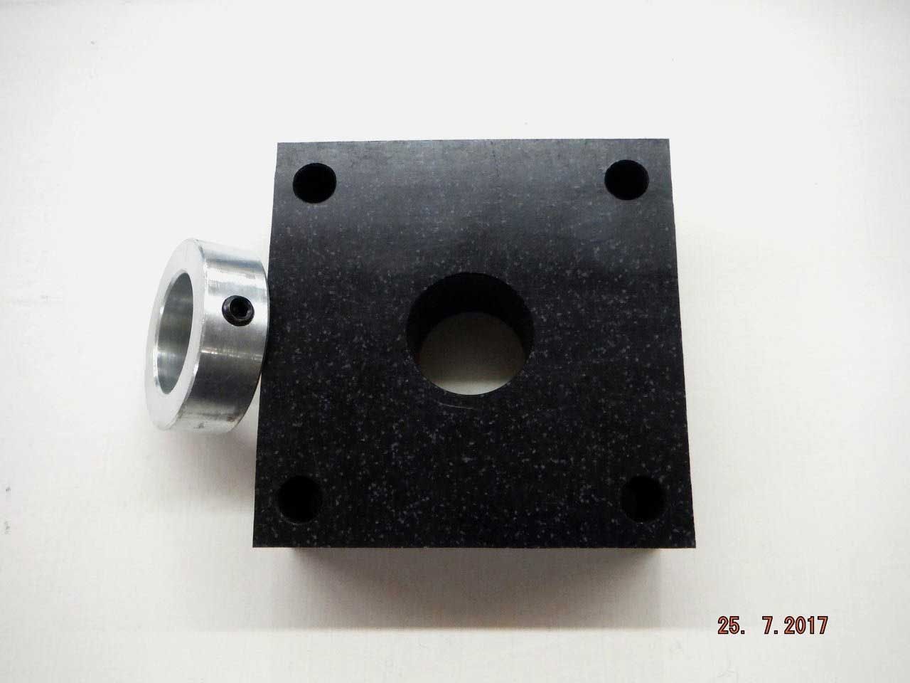 Black square mechanical part with a central hole and four corner holes, attached to a silver collar.