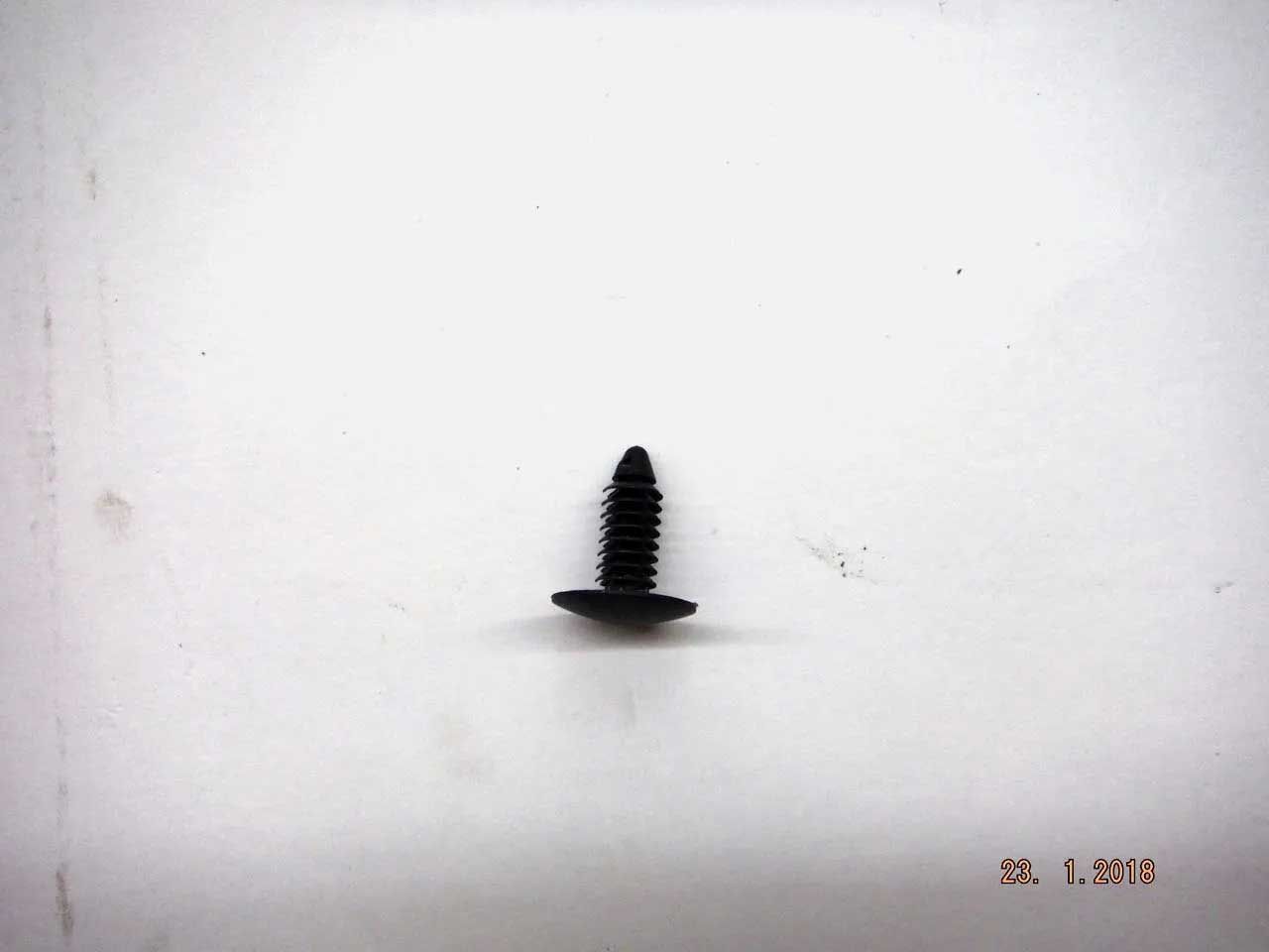 Black plastic fastener on a white surface. The fastener has a circular head and a ribbed post.