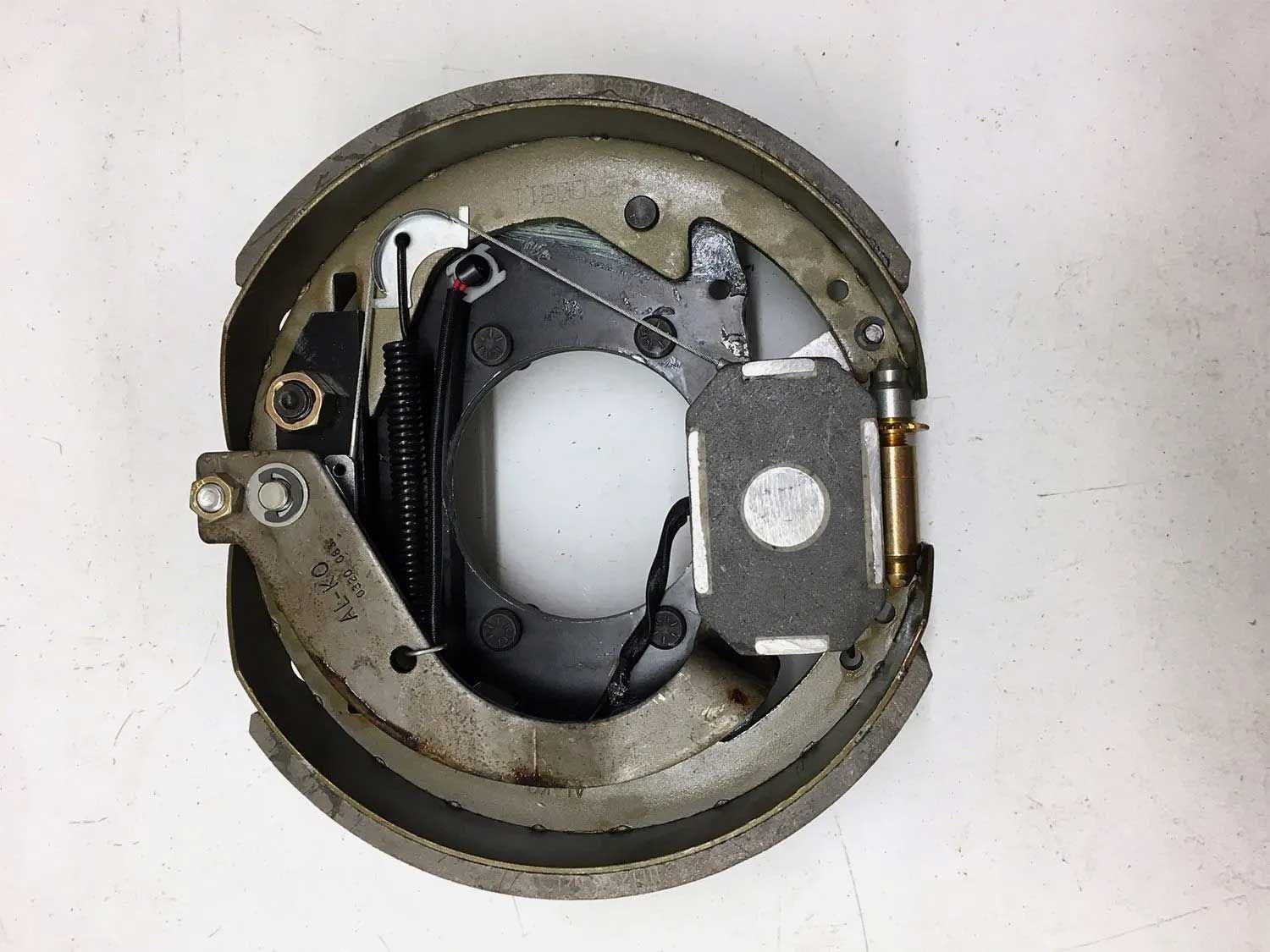 A drum brake assembly with metal components, including a circular backing plate and brake shoes, against a white backdrop.