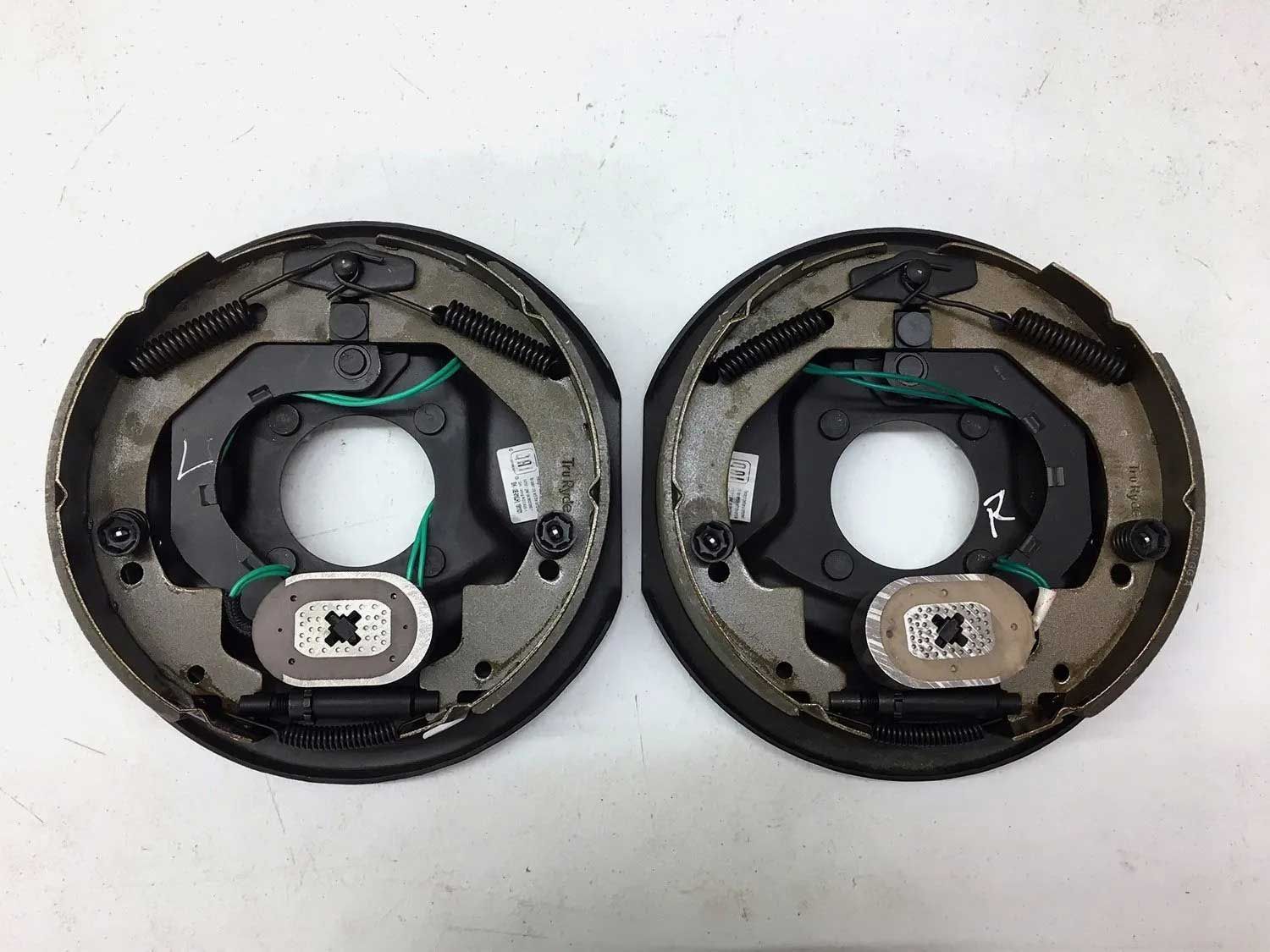 Two black trailer brake assemblies with metal brake shoes, electrical wiring, and mounting hardware.