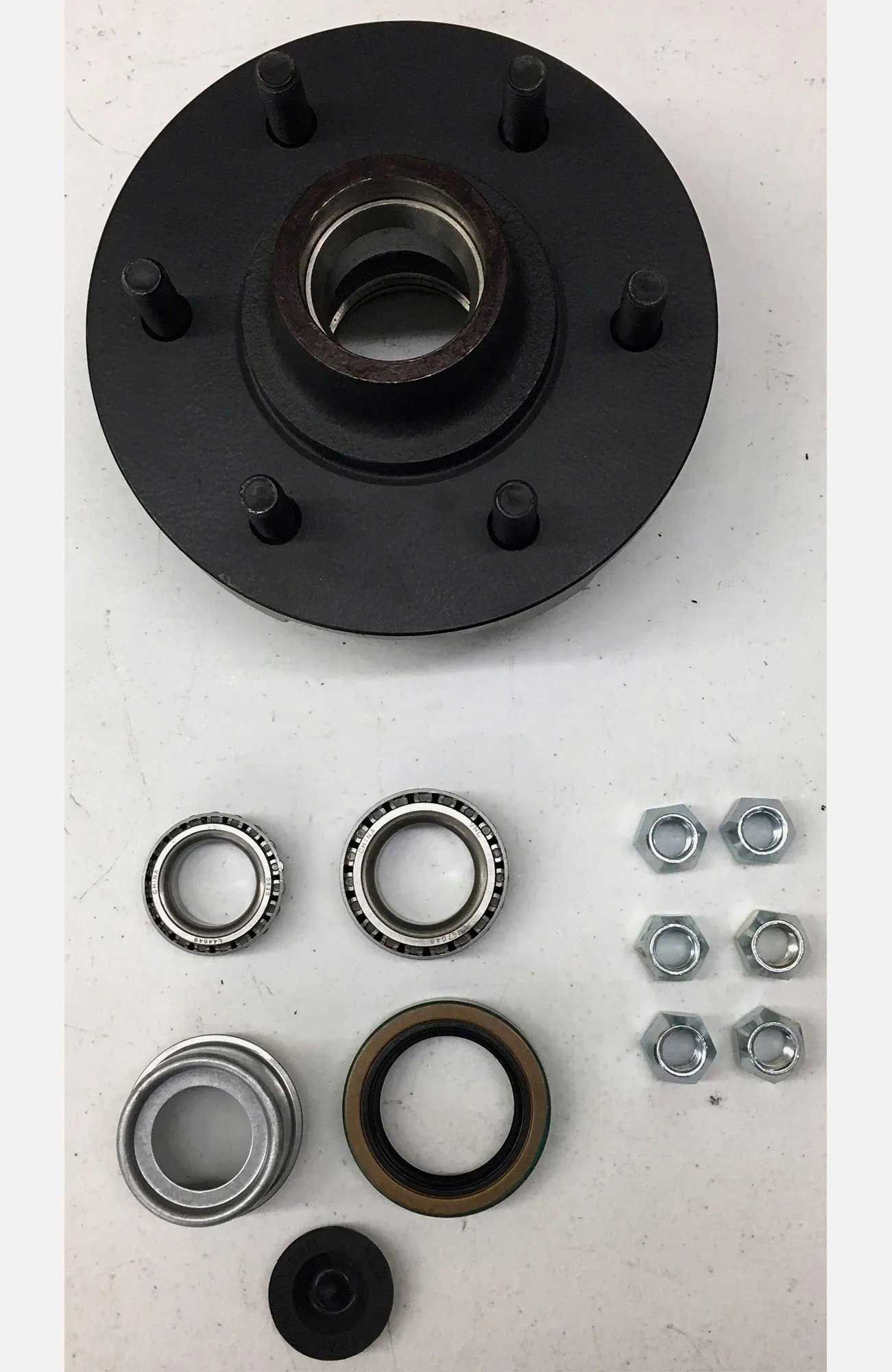 Black trailer hub with bearings, seals, and lug nuts laid out on a white surface, ready for assembly.