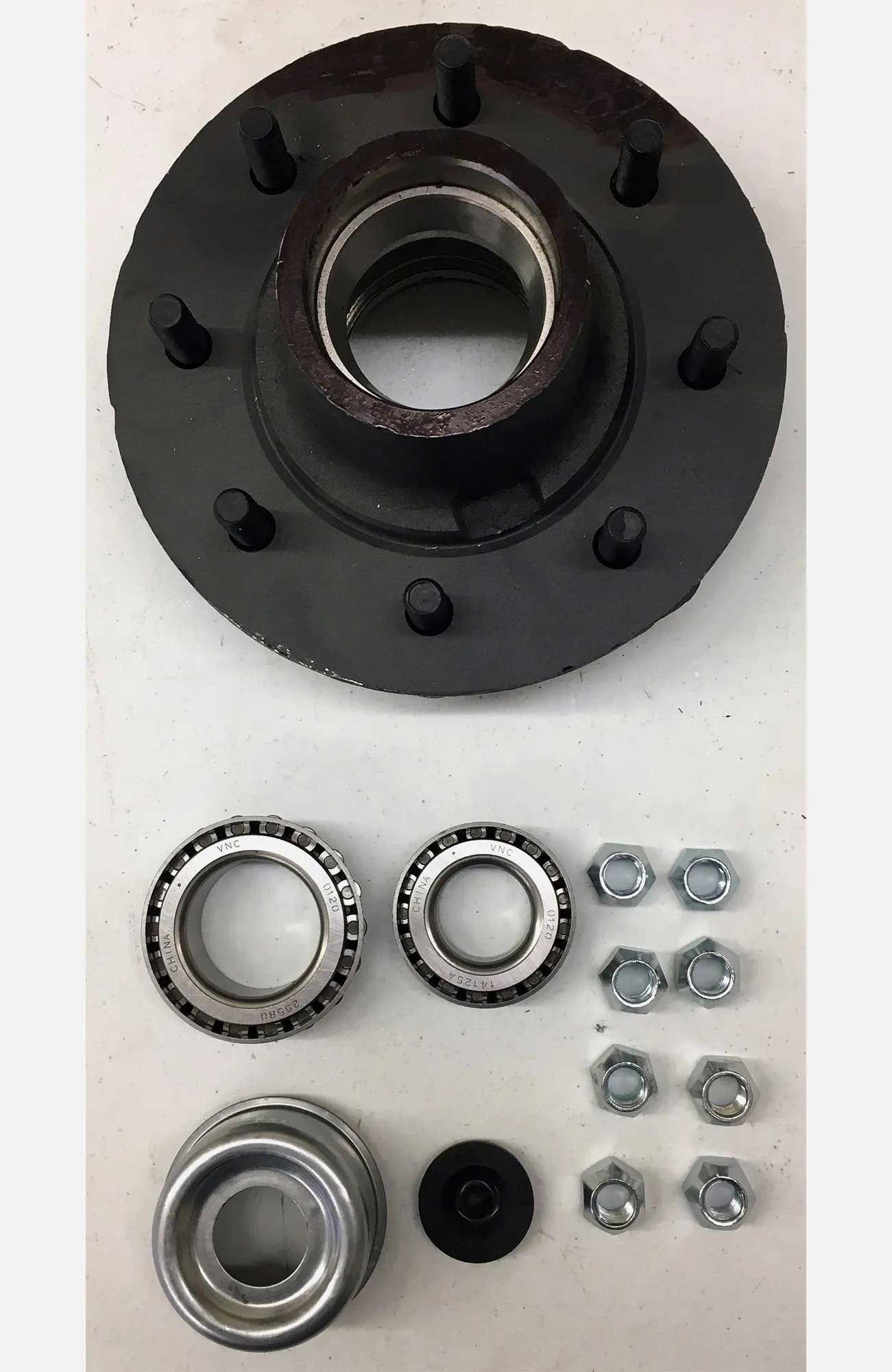 A black trailer hub with bearings, nuts, and other components laid out for assembly on a white surface.