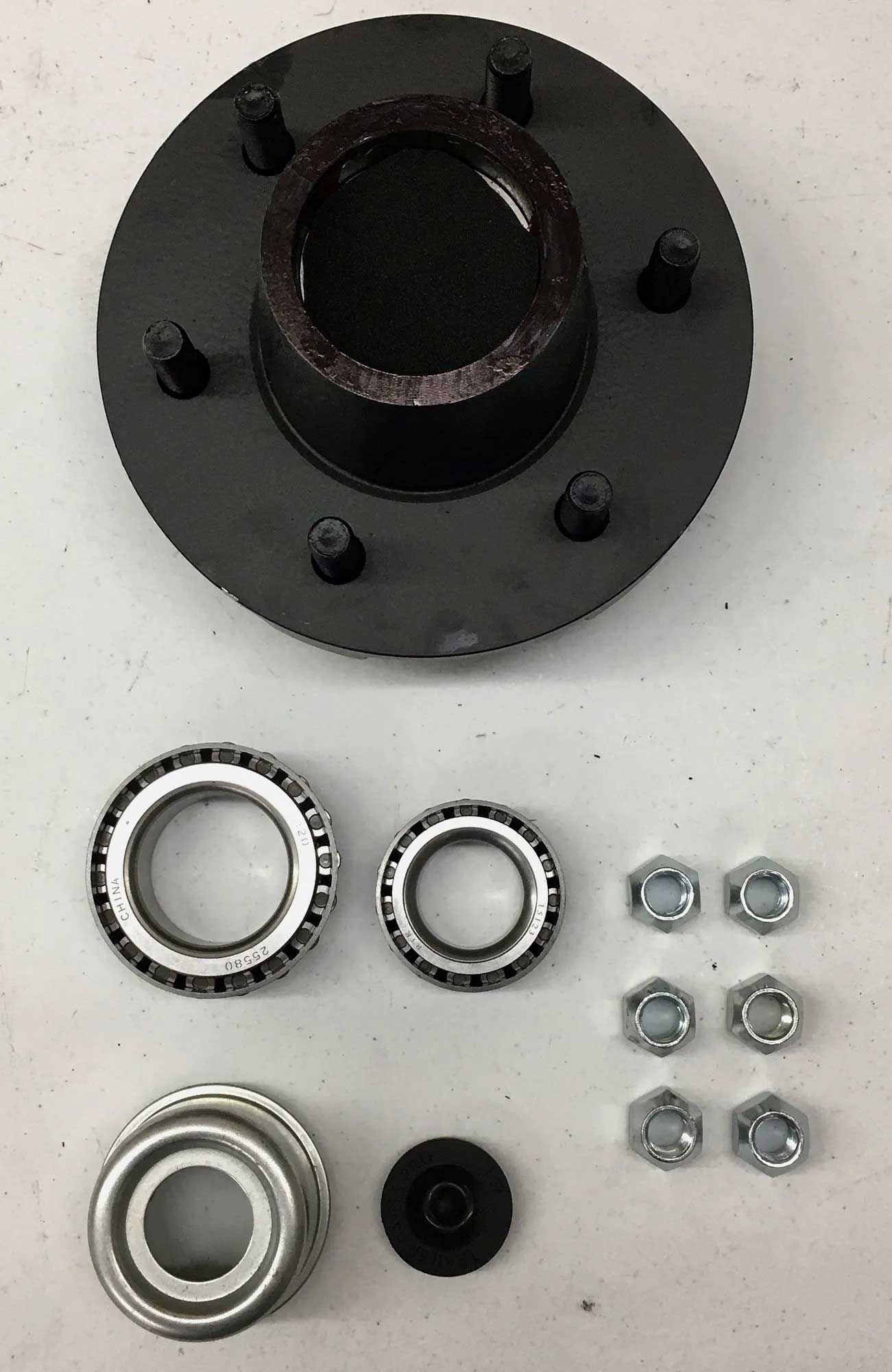 Black trailer hub, bearings, nuts, and other related parts laid out on a white surface.