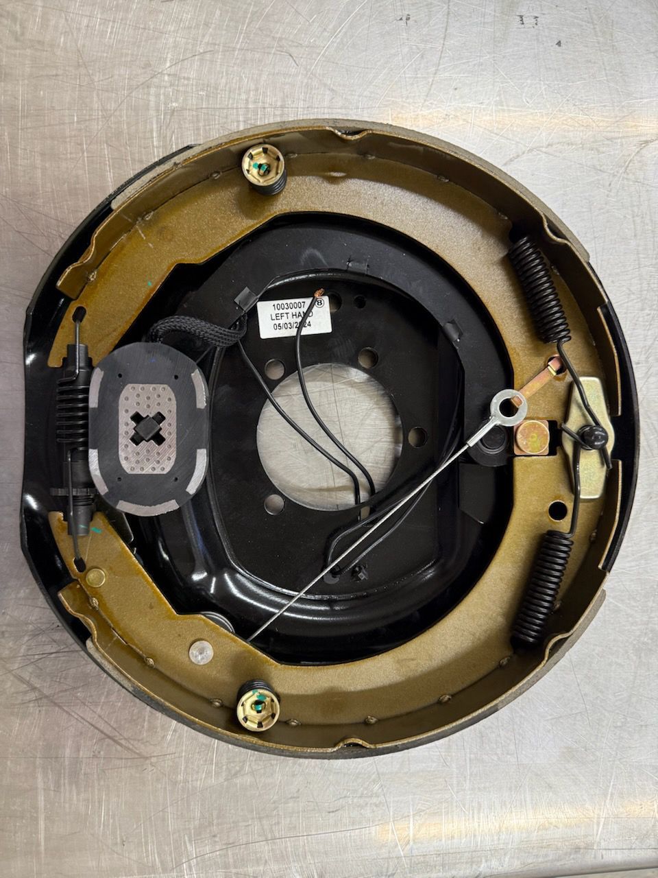 Black and gold trailer brake assembly. Brake shoes and springs inside a black backing plate.