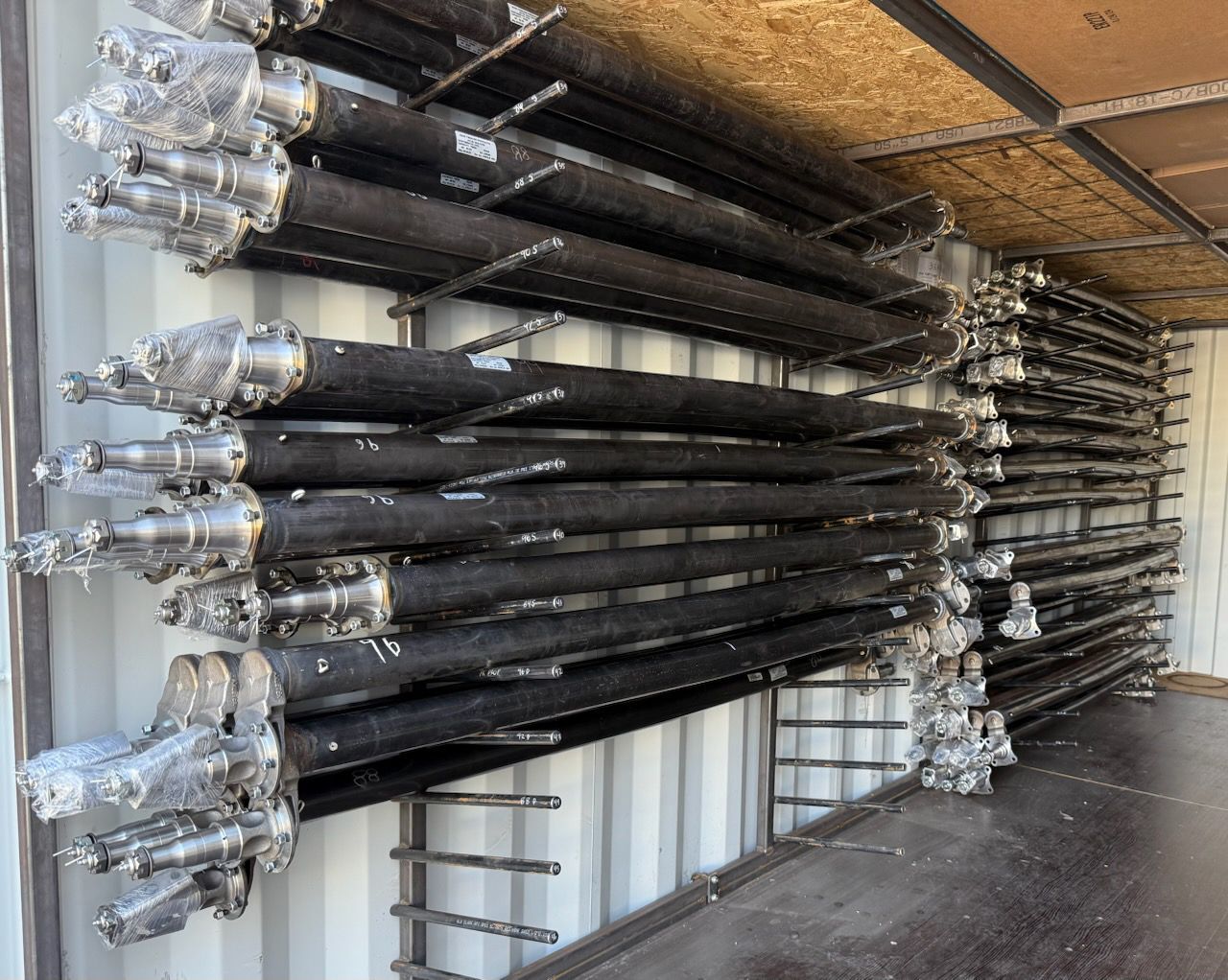 Racks of wrapped cylindrical metal parts stored inside a shipping container.