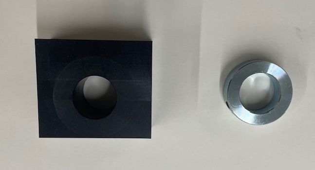 Dark blue square block and metallic washer with holes in the center, lying on a white surface.